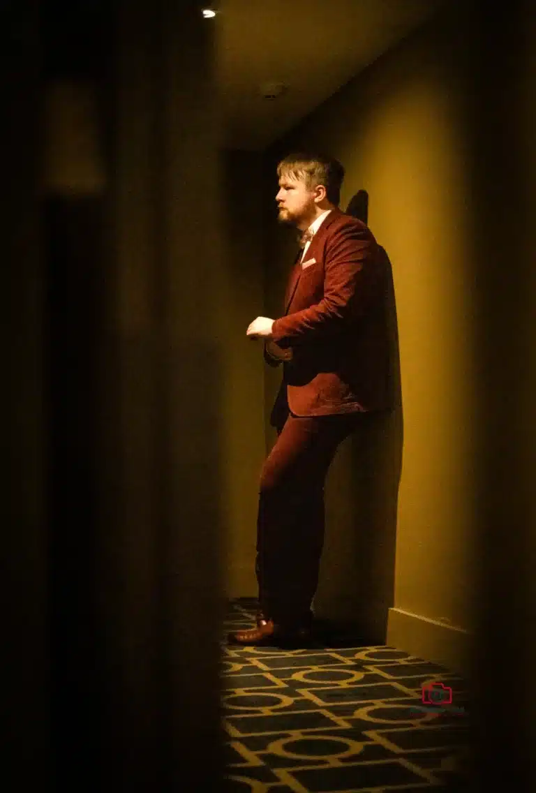 Groom standing alone in a dimly lit hallway, reflecting in a thoughtful pre-wedding moment