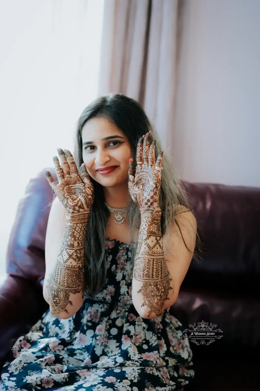 Smiling bride showcasing her intricate bridal mehndi designs on hands while wearing a floral dress, captured during a pre-wedding ceremony in Wellington by A Wedding Story