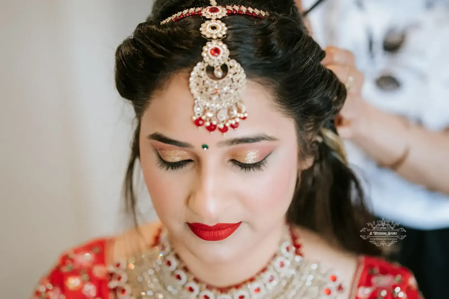 Indian bride in traditional red attire with golden makeup, wearing a maang tikka and red lipstick, captured during her wedding in Wellington by A Wedding Story