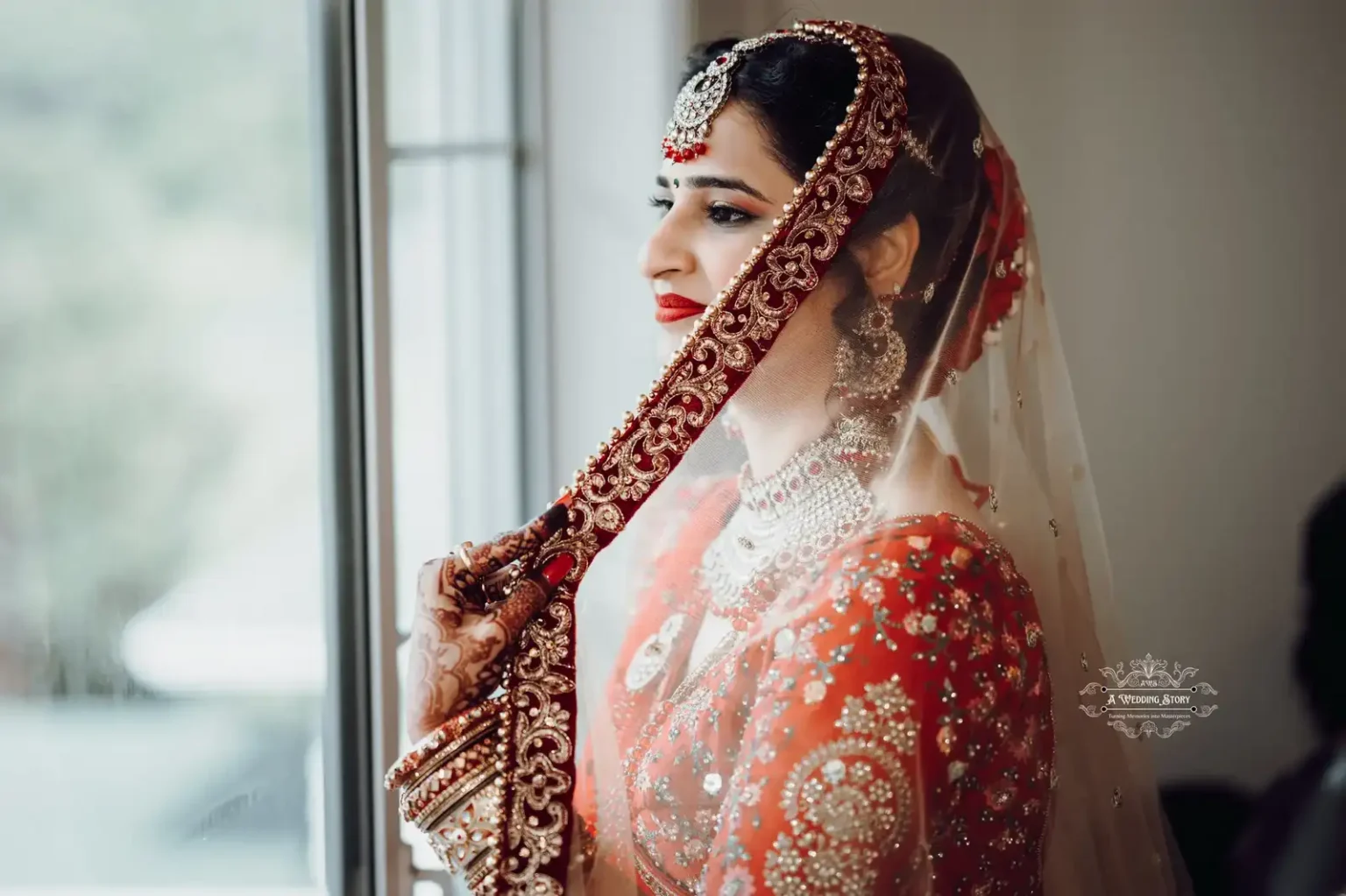 Indian bride in a red bridal outfit with intricate embroidery, adorned with traditional jewelry, looking out of a window in Wellington, NZ.