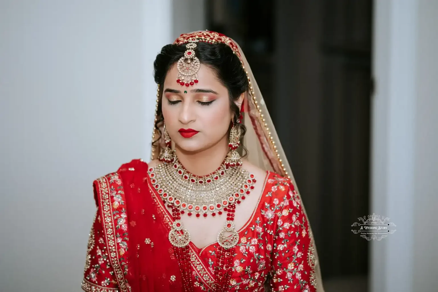 Indian bride in red and gold traditional attire with intricate jewelry, eyes closed in a serene moment before the wedding ceremony.