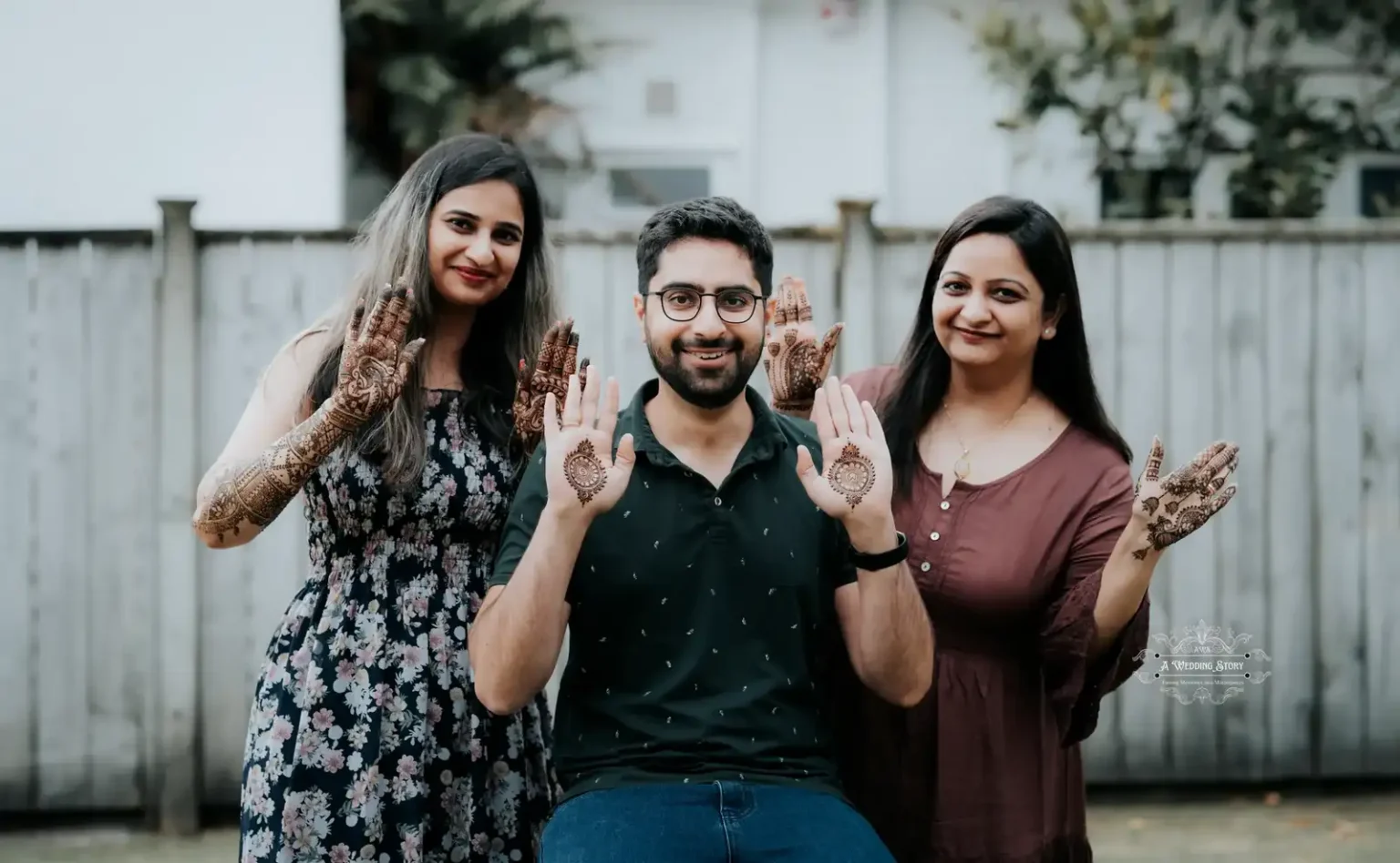 Smiling groom showcasing mehndi designs on his palms alongside the bride and a family member, during a joyful pre-wedding celebration in Wellington by A Wedding Story