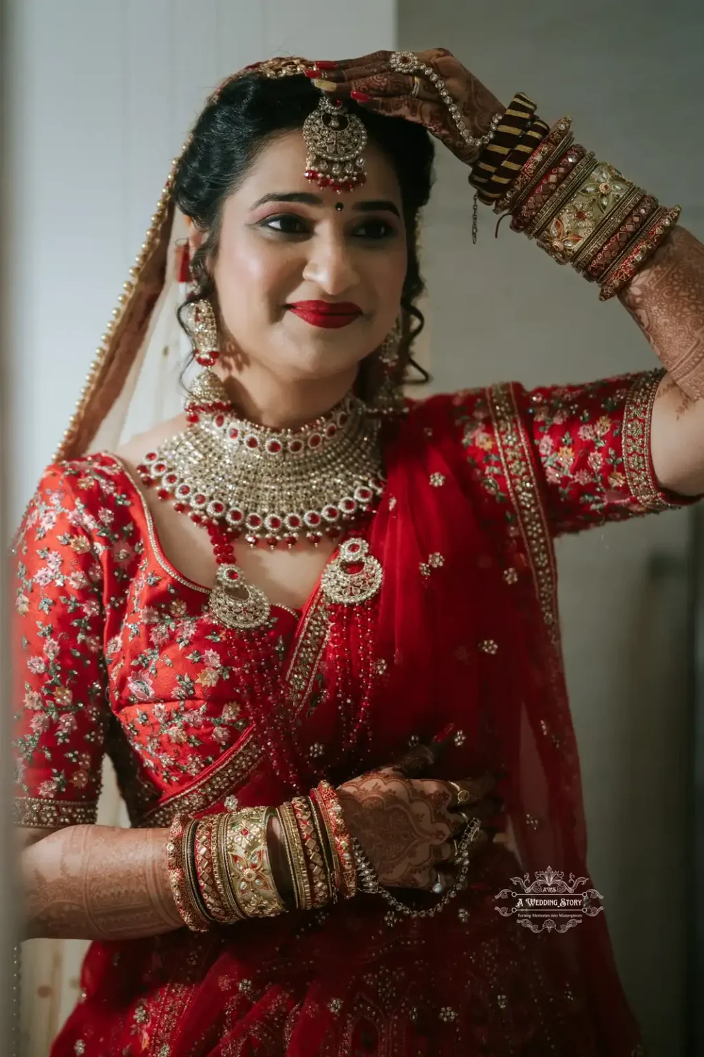 Beautiful bride wearing traditional red attire and intricate jewelry, adjusting her bridal headpiece with a joyful smile.