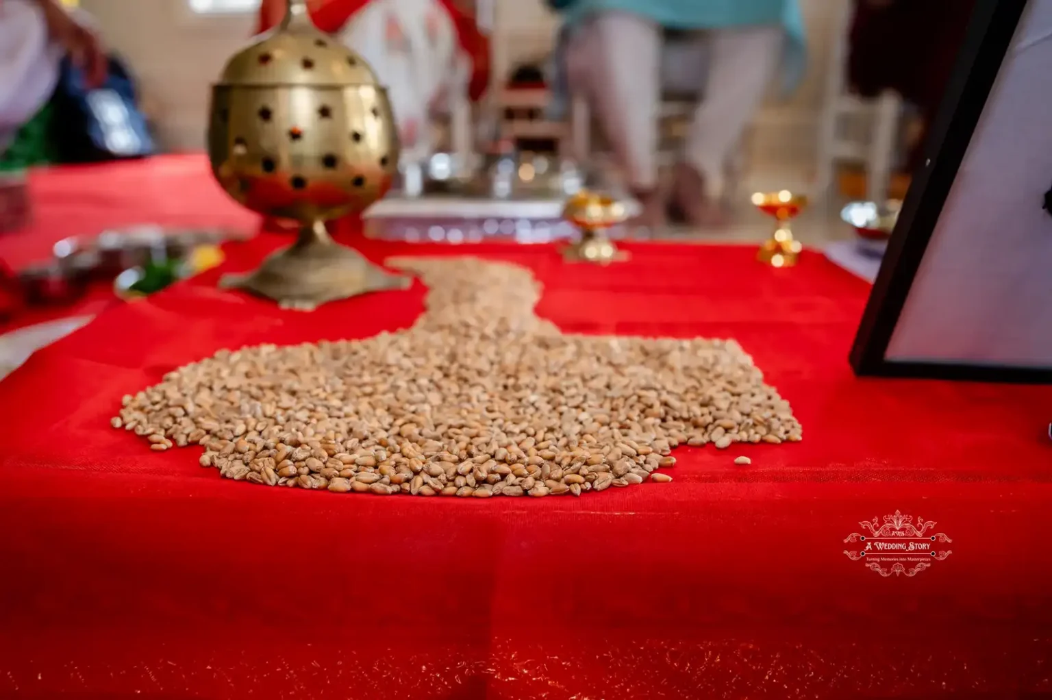 A close-up of a sacred grain arrangement on a red cloth, with traditional brass items in the background, used in a wedding ceremony.