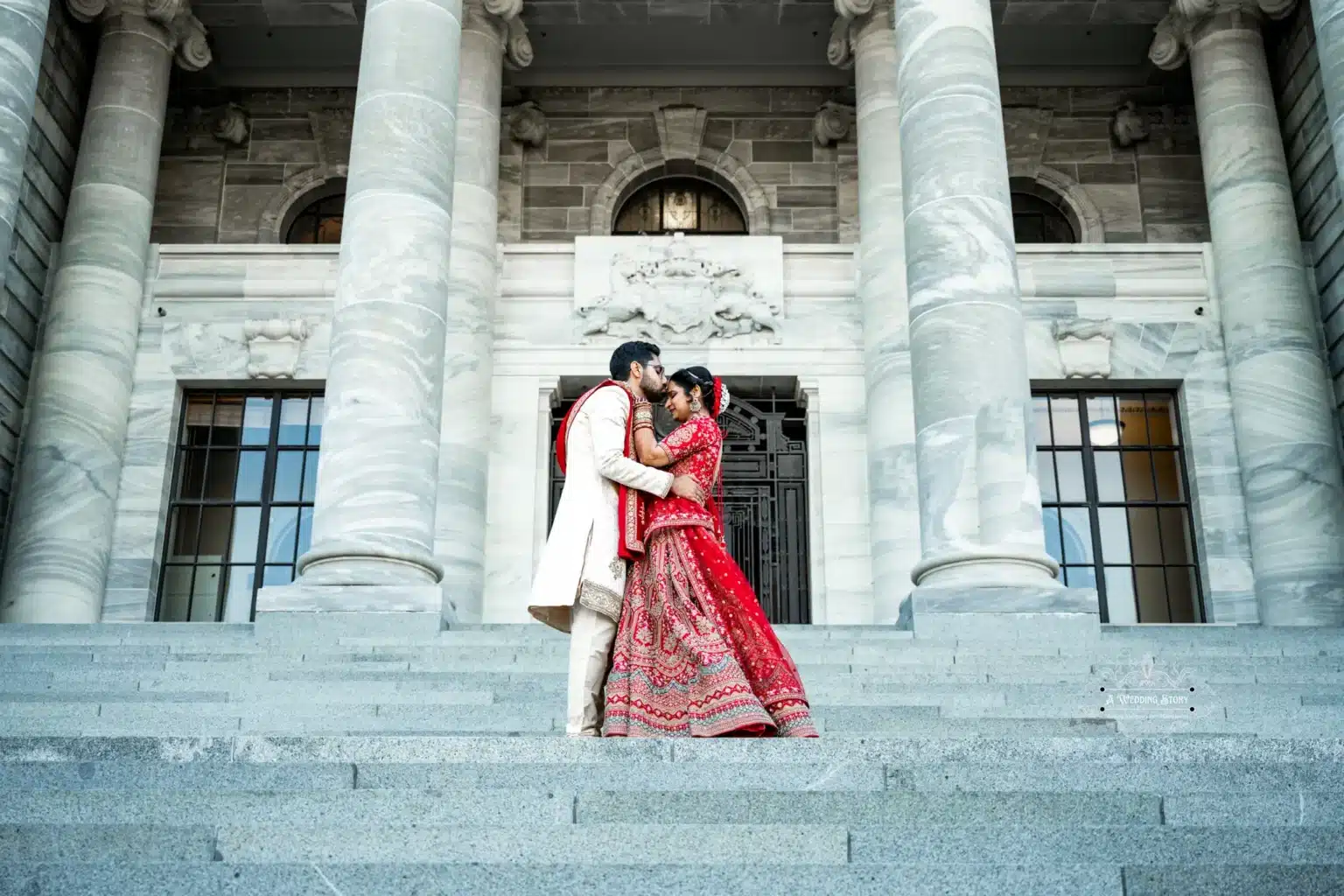 Bride and groom in traditional Indian attire sharing an intimate moment on the Parliament steps in Wellington, New Zealand.