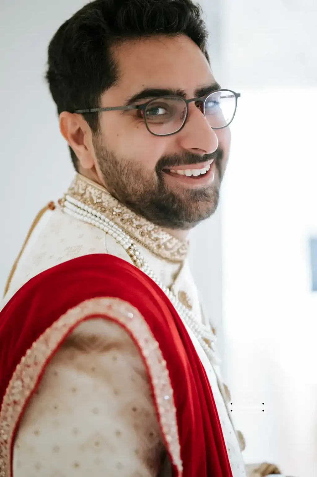 Indian groom smiling in traditional wedding attire with a red shawl, captured in Wellington by Wedding Photography.