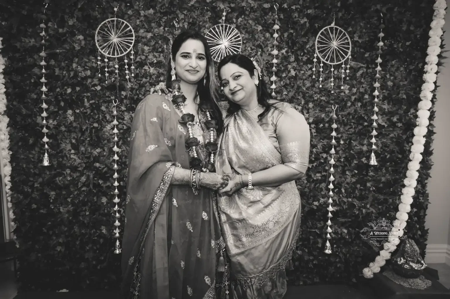 A black-and-white photo of two women in traditional attire posing together with a backdrop of ceremonial decorations, symbolizing friendship and togetherness.