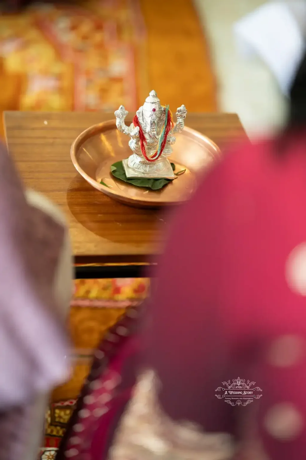 Close-up of hands performing a cultural water ritual in a wedding, with water poured from a copper vessel over a deity statue placed on a tray.