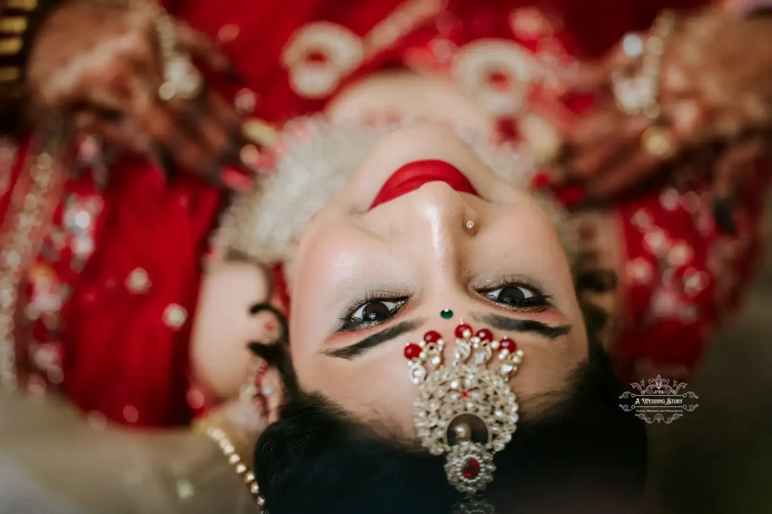 Close-up of a bride looking upward with intricate jewelry, bright red lipstick, and captivating eyes, lying back in traditional attire.