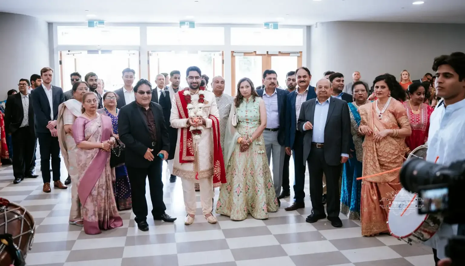 The groom, dressed in traditional attire, stands at the center of a large family gathering during a wedding ceremony in Wellington.