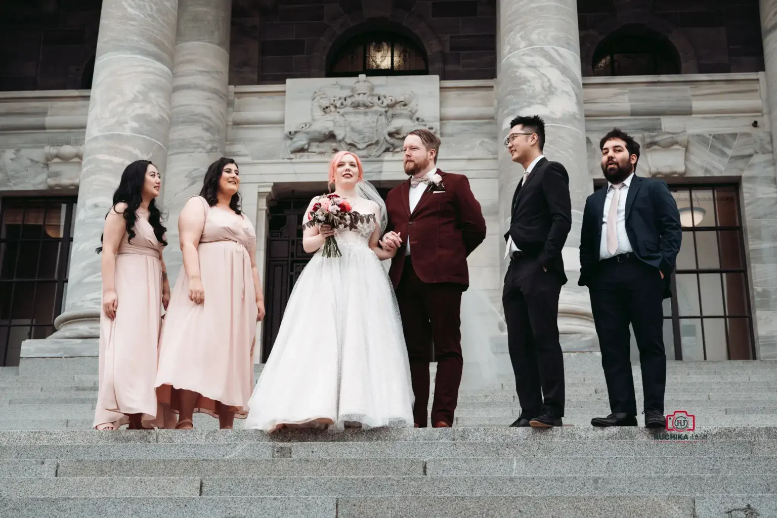 Bride, groom, and bridal party standing on the stone steps of a historic building with large columns.