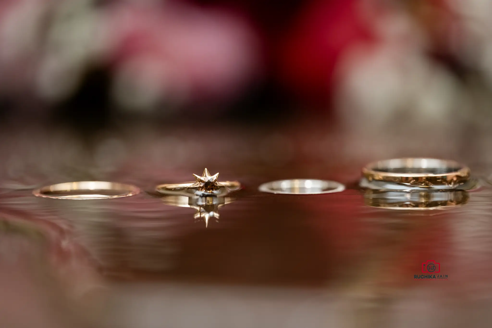 Close-up of wedding rings, including a star-shaped engagement ring, reflecting on a smooth surface with a blurred background