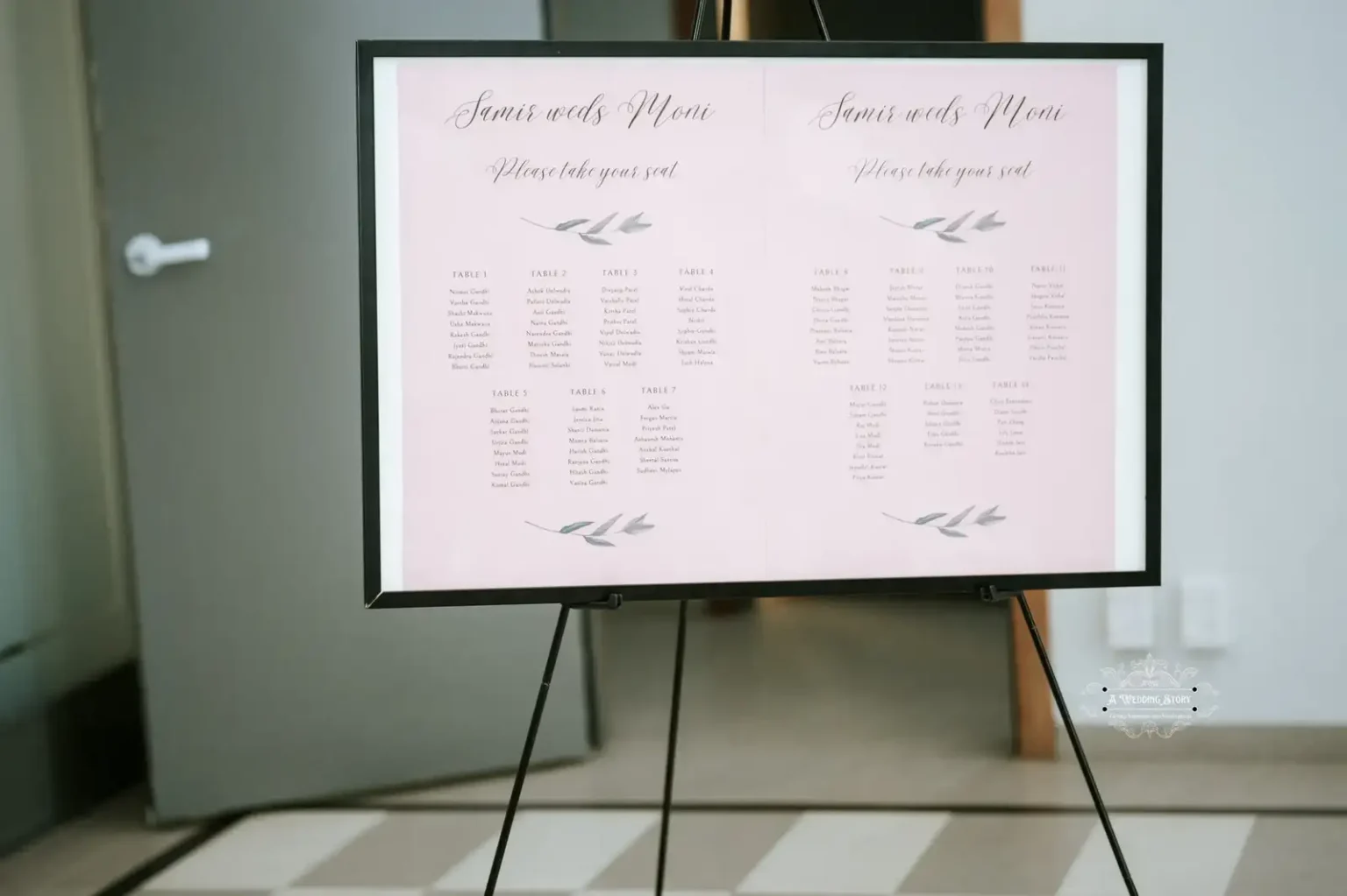 Wedding seating chart display for Samir and Moni's reception with a soft pink background, showing guest seating arrangements for each table.