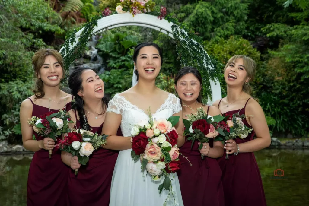 A cheerful bride and her bridesmaids holding floral bouquets, sharing laughter during a garden wedding in Wellington, New Zealand.