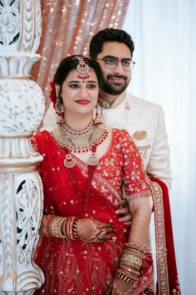 Bride in red traditional attire and groom in white sherwani share a joyful moment together during the wedding.