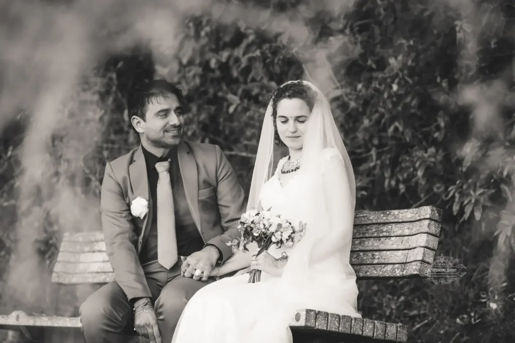 A black-and-white wedding portrait of a bride and groom seated on a bench, sharing a serene and intimate moment in a natural setting