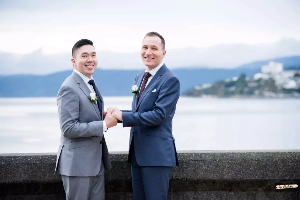 A joyful couple in elegant suits celebrating their wedding with a scenic waterfront backdrop in Wellington, New Zealand