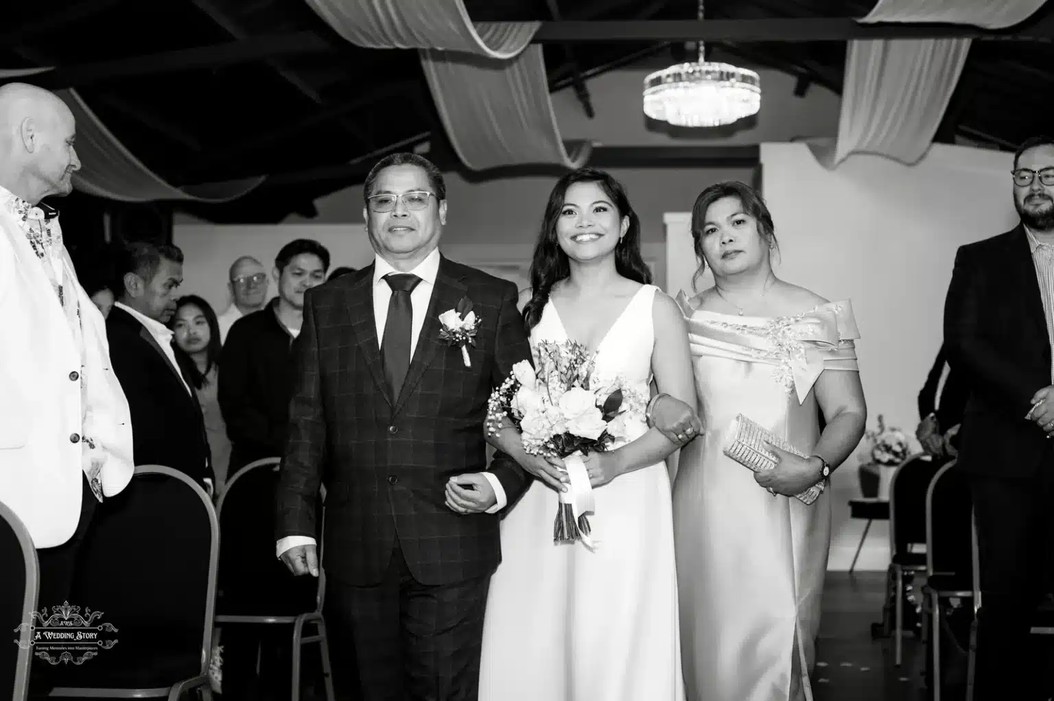 A radiant bride walking down the aisle with her parents in a black-and-white photograph, capturing a timeless moment filled with elegance and emotion during a Wellington wedding ceremony.