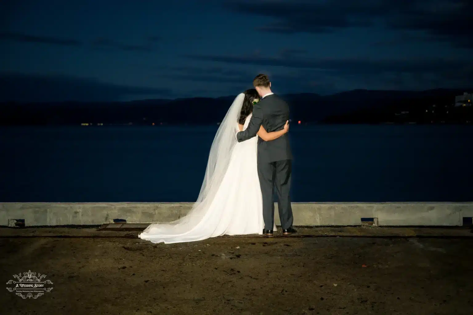 Bride and groom embracing at night by the waterfront in Wellington