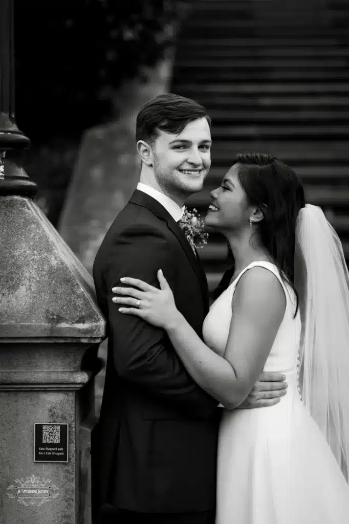 Bride and groom sharing a loving moment by a staircase in a black-and-white wedding portrait