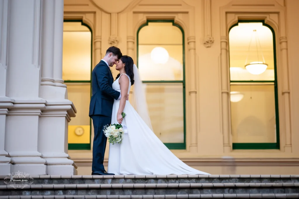 A bride and groom embracing on the steps of a historic building in Wellington, New Zealand, with soft evening light highlighting the scene.