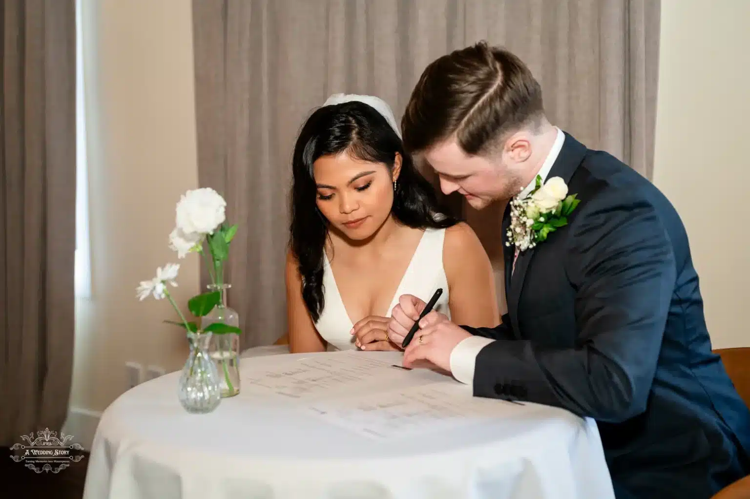 Bride and groom signing their marriage certificate at a round table with white flowers in Wellington, New Zealand.