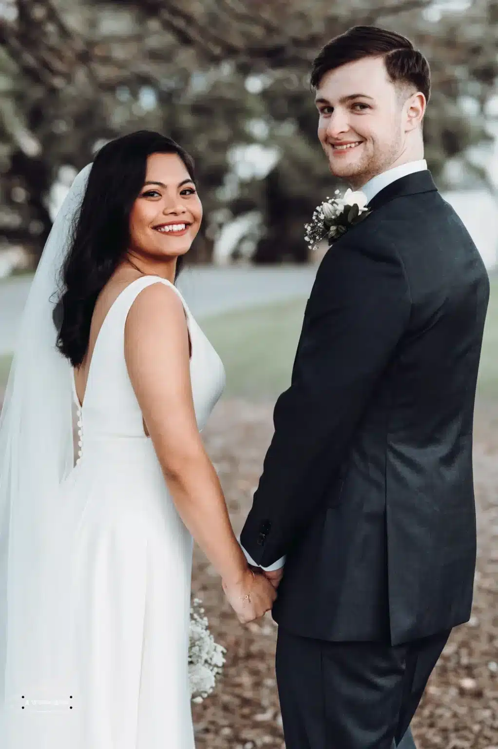 Bride and groom holding hands, smiling back towards the camera, framed by Wellington’s serene natural setting.