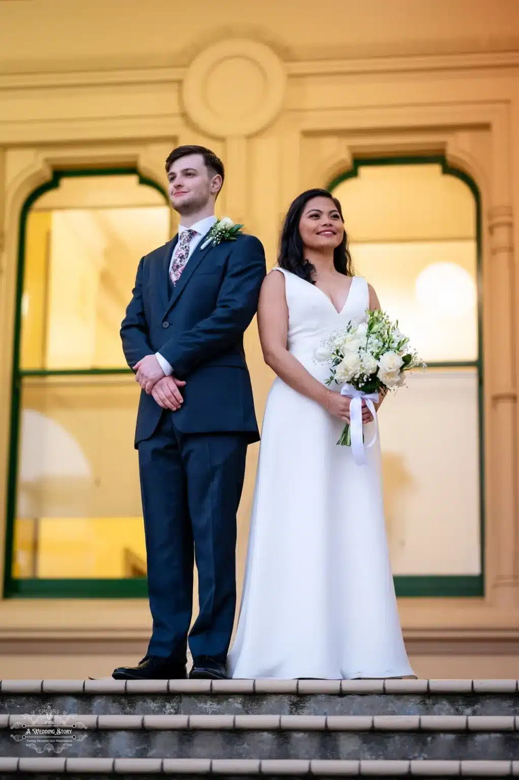 Bride and groom in formal attire standing on steps of a historic building in Wellington.