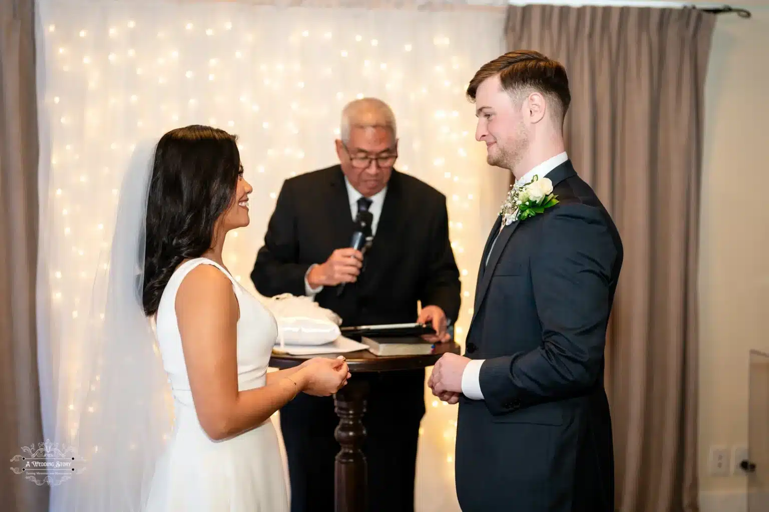 Bride and groom standing face-to-face during a heartfelt vow exchange, with the officiant leading the ceremony under glowing fairy lights.