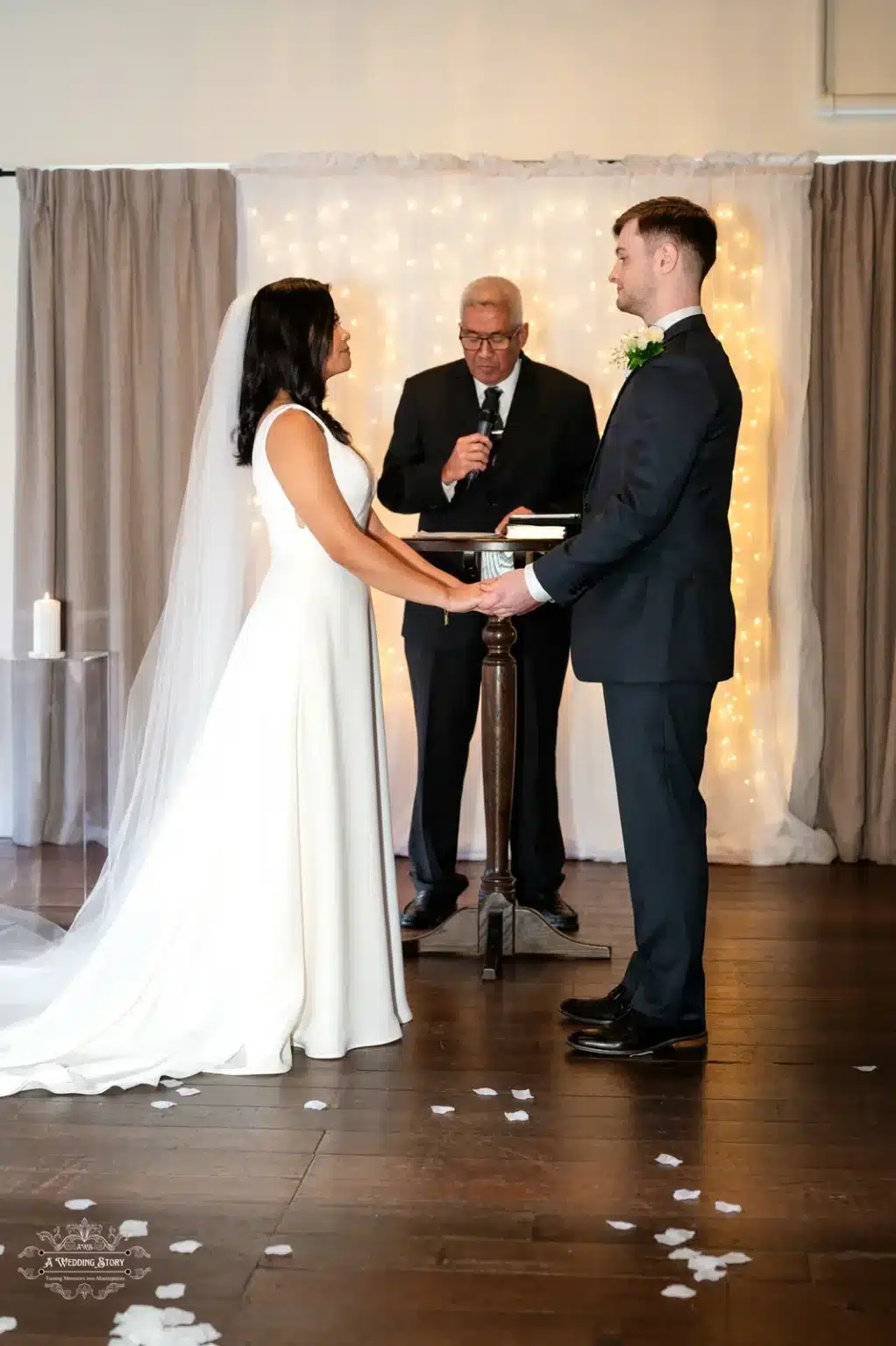 The bride and groom hold hands and exchange heartfelt vows during their intimate wedding ceremony in Wellington, illuminated by soft fairy lights in the background.