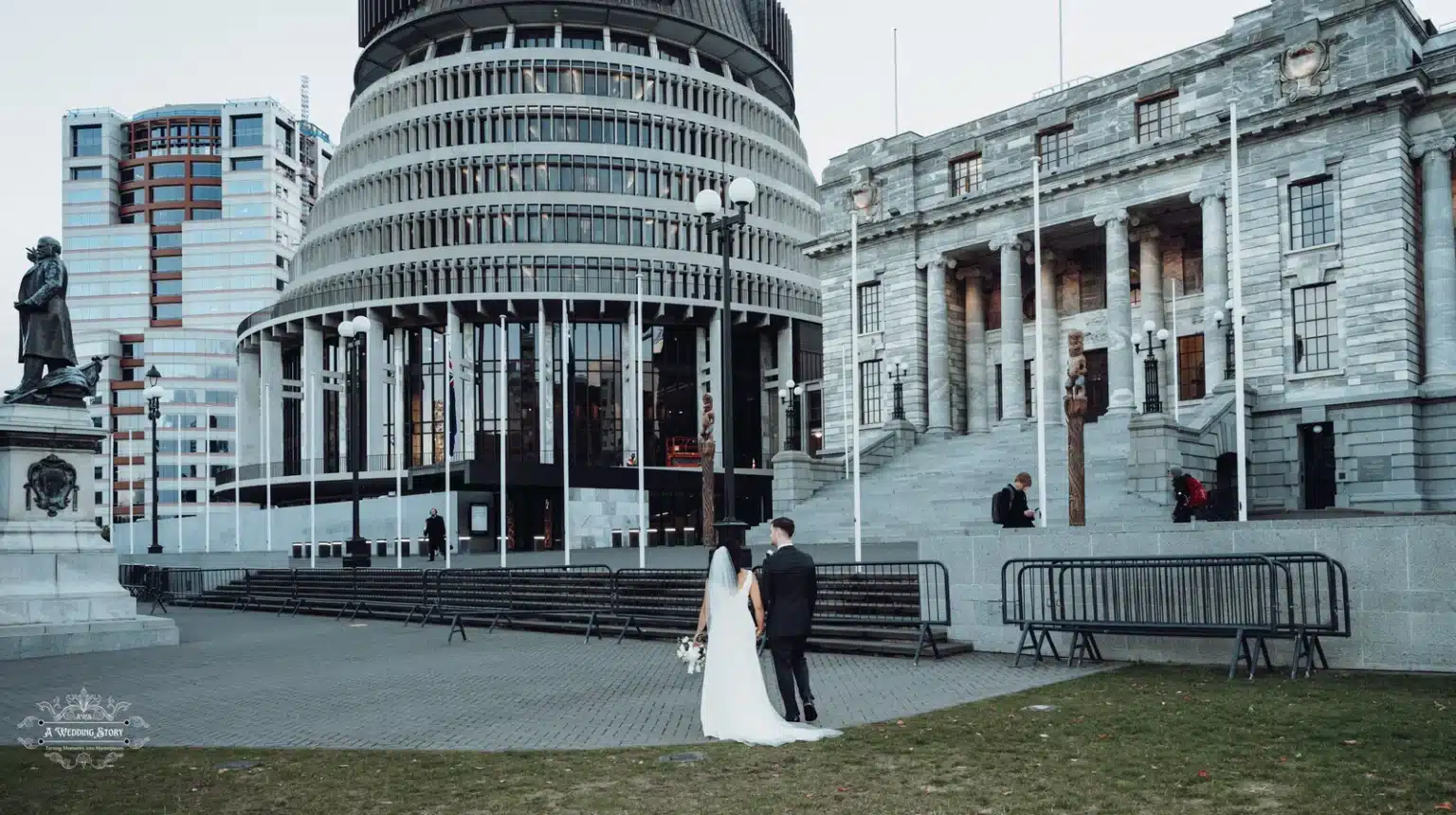 Bride and groom walking hand in hand in front of Wellington’s historic Parliament buildings, framed by urban architecture.