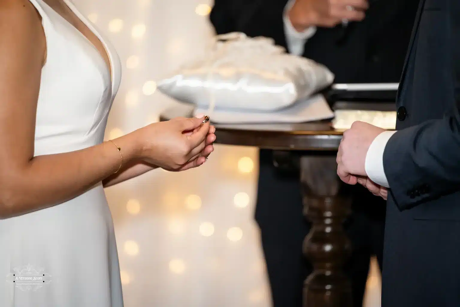 Close-up of a bride holding a wedding ring during a heartfelt exchange of vows, with soft glowing lights in the background.