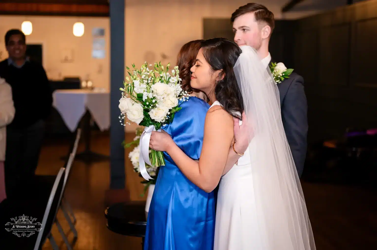 Bride embracing her mother during the wedding ceremony, holding a white floral bouquet, with the groom standing close in Wellington, New Zealand.