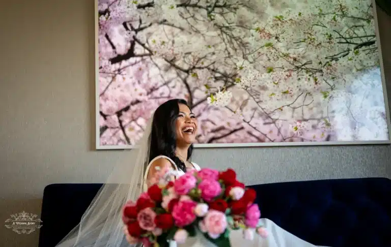 A radiant bride laughing joyfully, seated beneath a cherry blossom painting, with vibrant floral arrangements in the foreground, capturing a serene moment in Wellington, New Zealand.