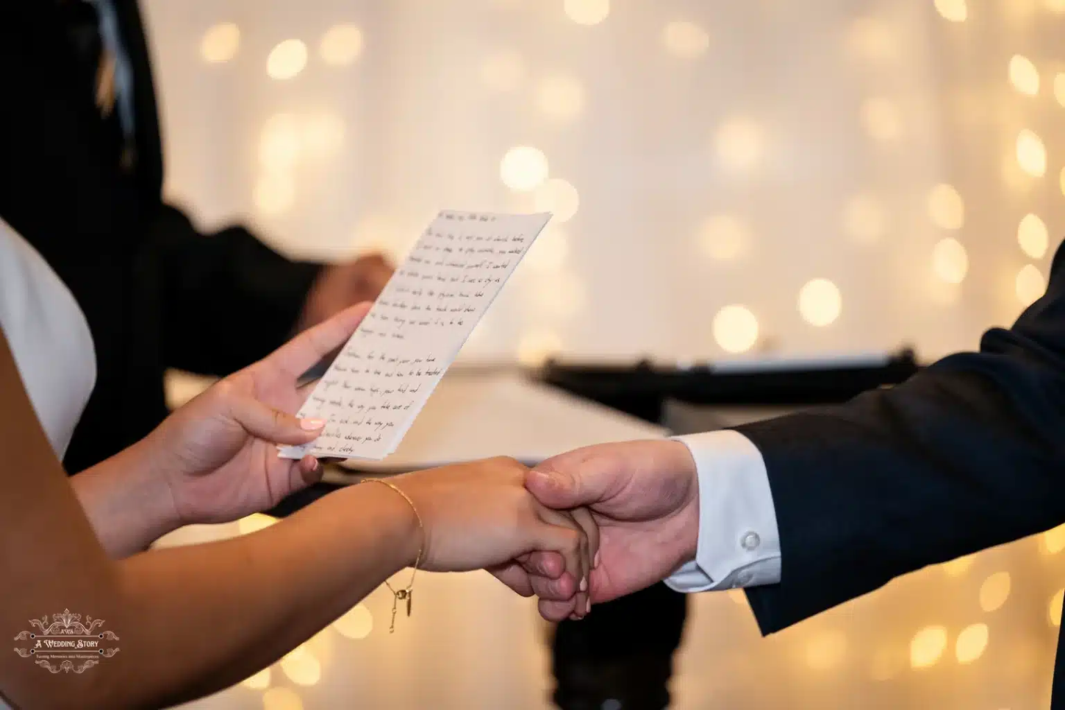 Bride holding a written vow card and the groom’s hand during an emotional wedding ceremony with glowing lights in the background.