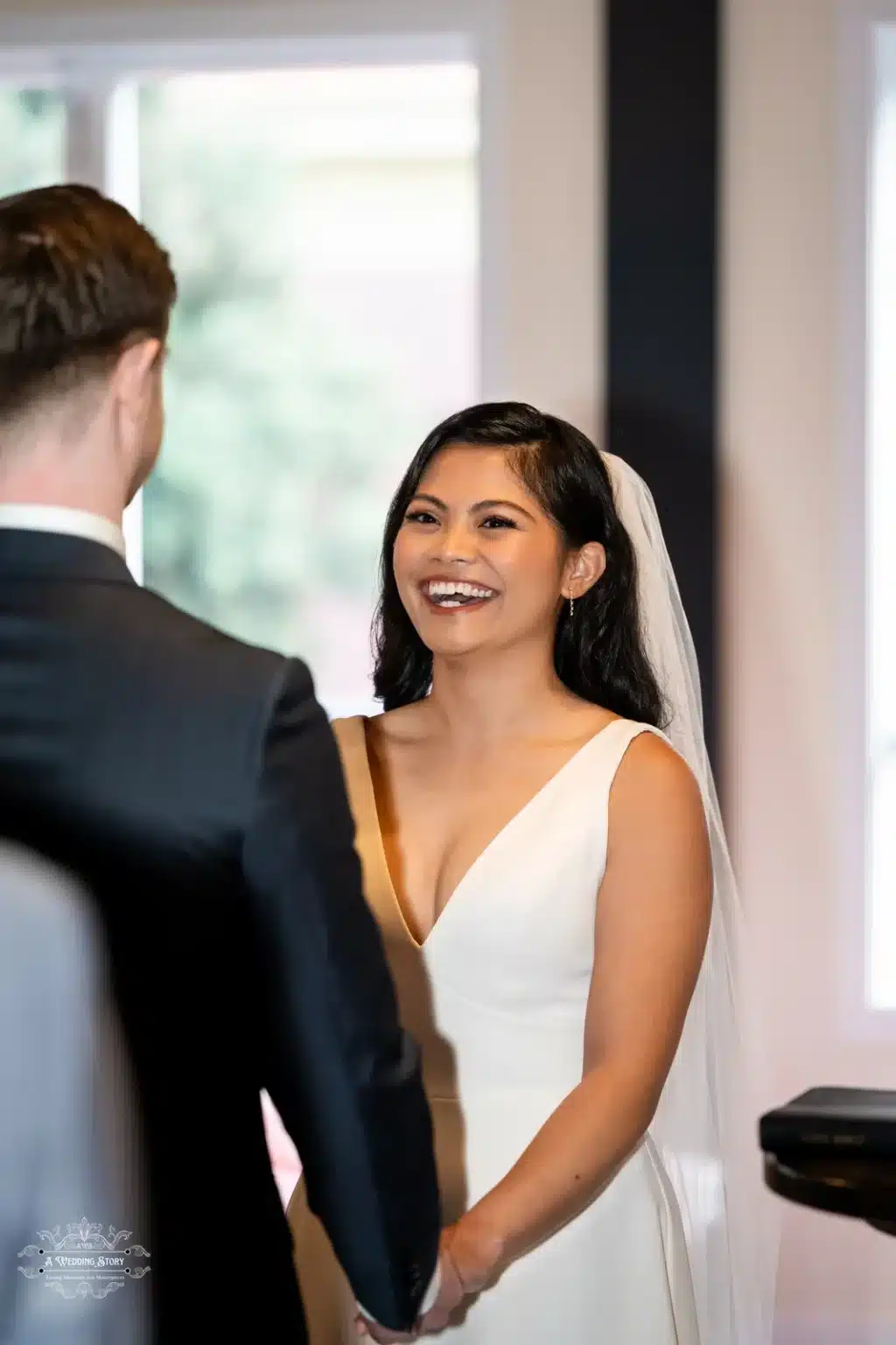 A close-up of the bride smiling brightly as she holds her groom's hands during their wedding ceremony, showcasing her happiness and love.