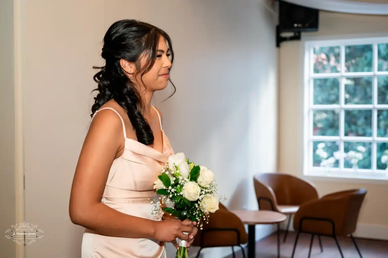 A close-up of a bridesmaid holding a bouquet of white roses and greenery, dressed in a blush pink gown during a Wellington wedding ceremony.