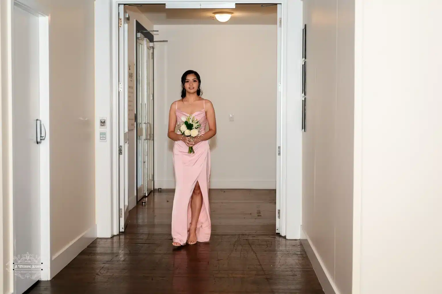 A bridesmaid in a blush pink gown walking down the aisle holding a bouquet at a wedding ceremony in Wellington, New Zealand.