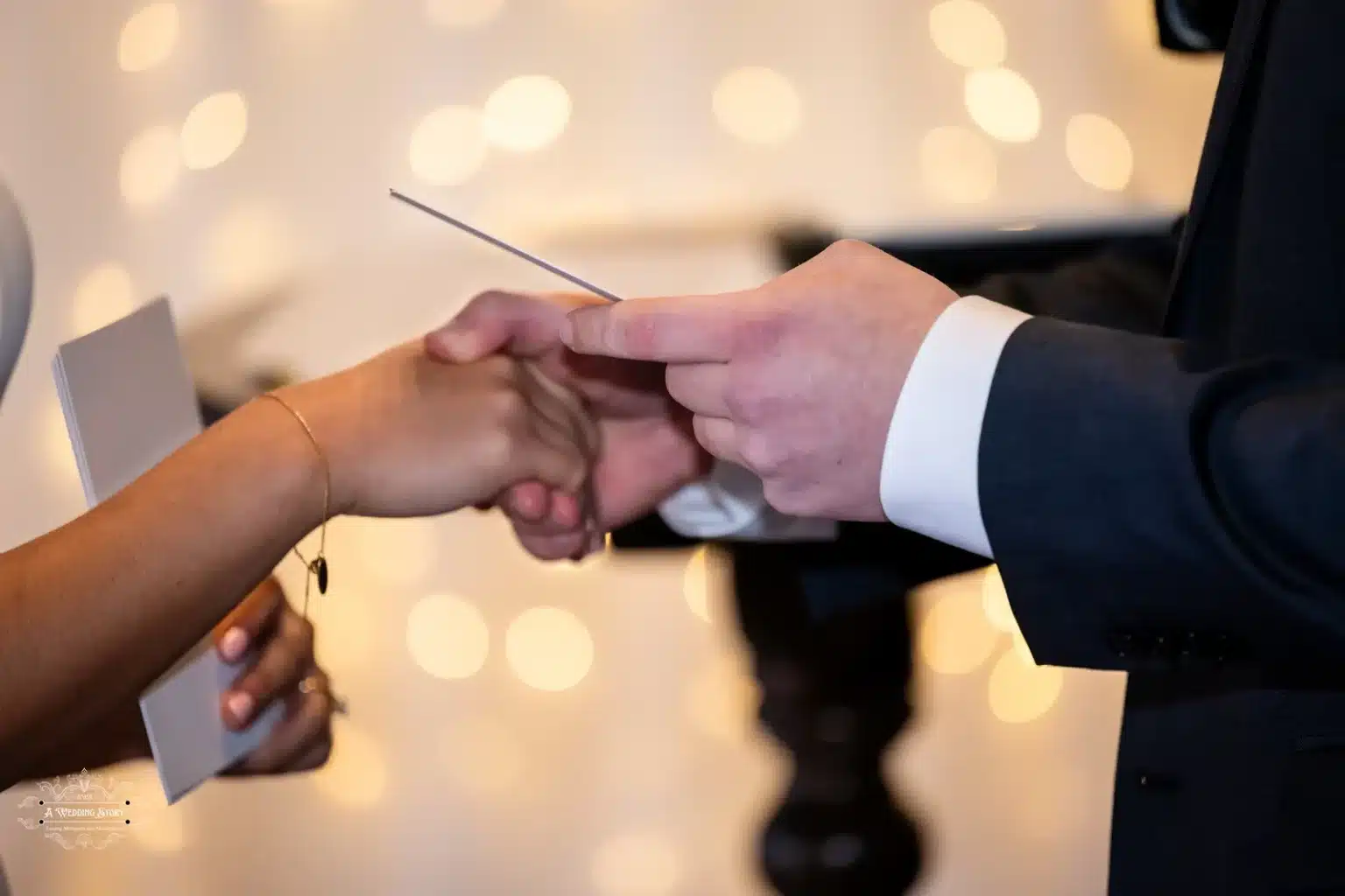 Close-up of a couple exchanging vows, showcasing hands holding cards with a romantic bokeh background during a wedding in Wellington.