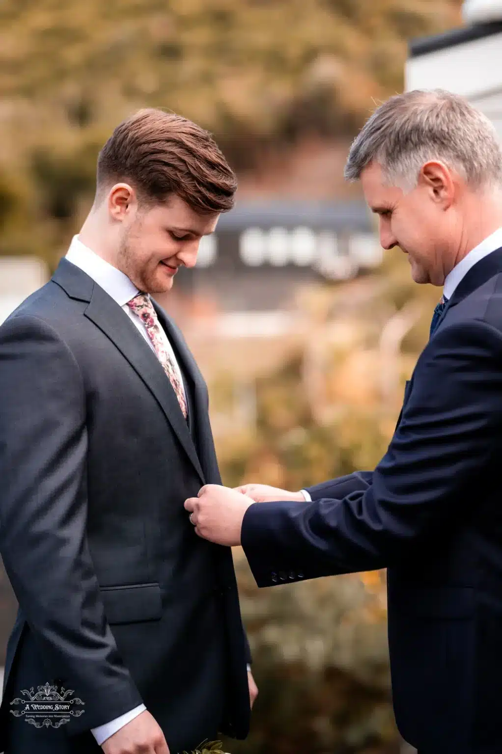 Father assisting groom with his suit jacket before the wedding ceremony, a candid outdoor moment in Wellington, New Zealand.