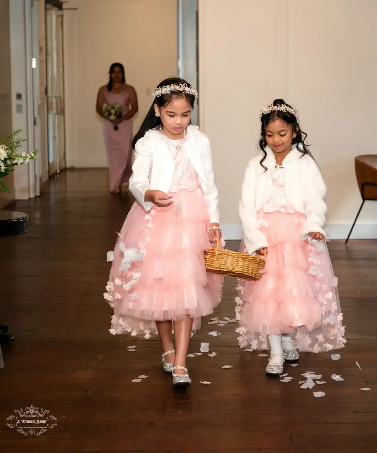 Two flower girls dressed in pink tulle dresses walking down the aisle, spreading petals during a wedding ceremony in Wellington, New Zealand.