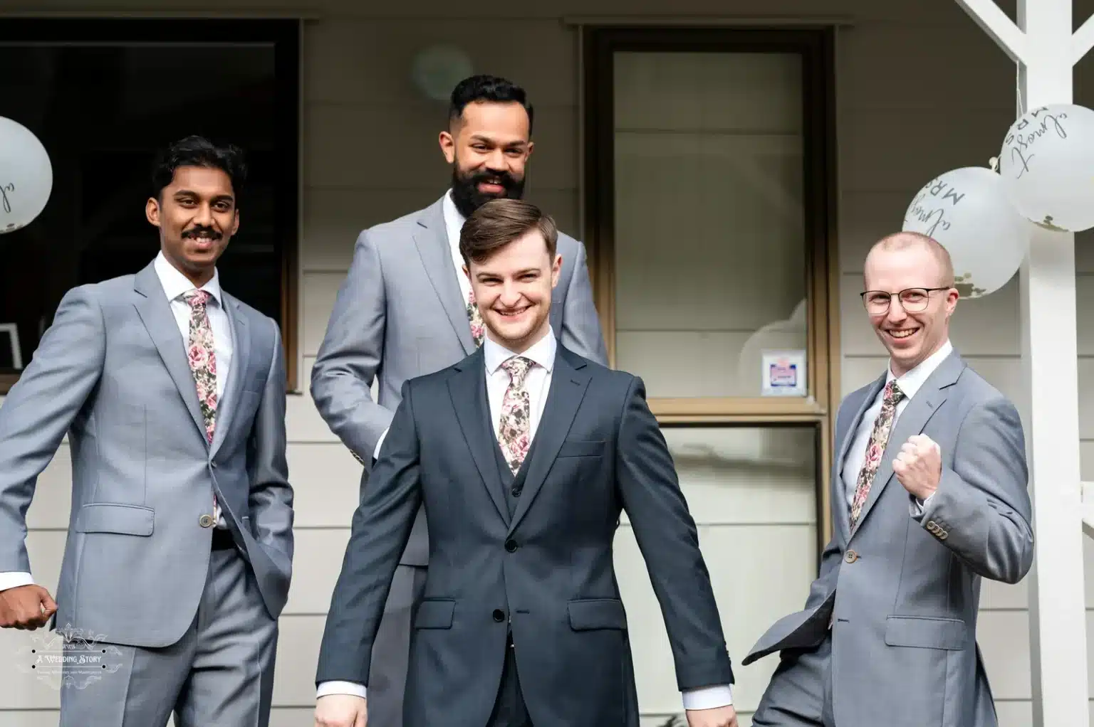 The groom and his three groomsmen pose confidently in coordinated grey suits with floral ties before a wedding ceremony in Wellington.