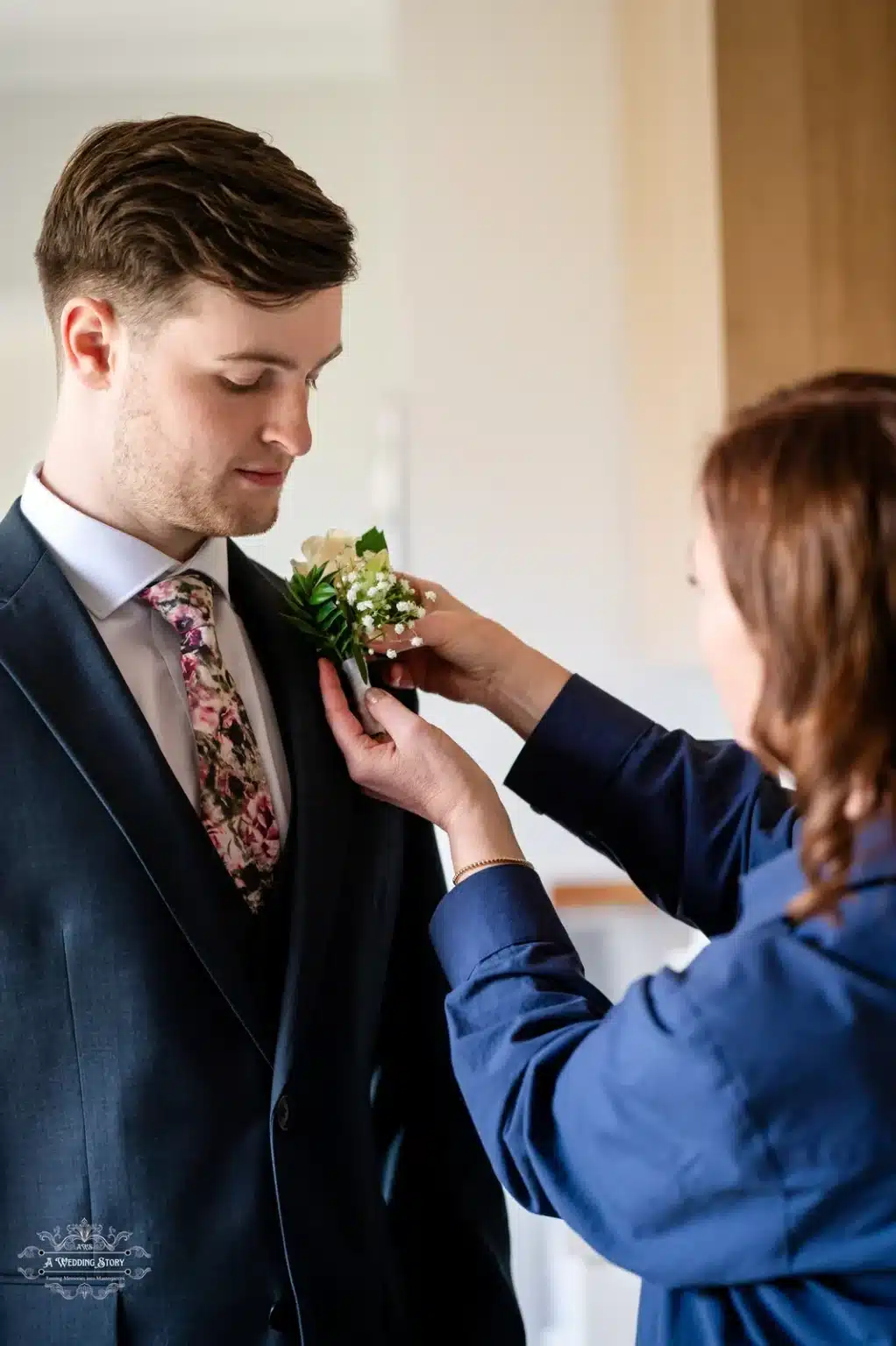 Groom getting his boutonniere pinned by a family member before the wedding ceremony, showcasing a heartfelt preparation moment.