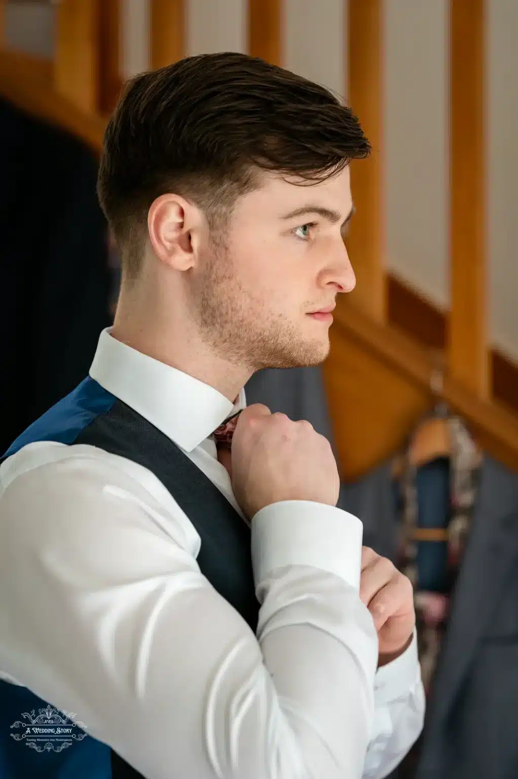 A focused groom adjusting his tie while getting ready for his wedding day in Wellington, New Zealand, wearing a white shirt and navy vest.