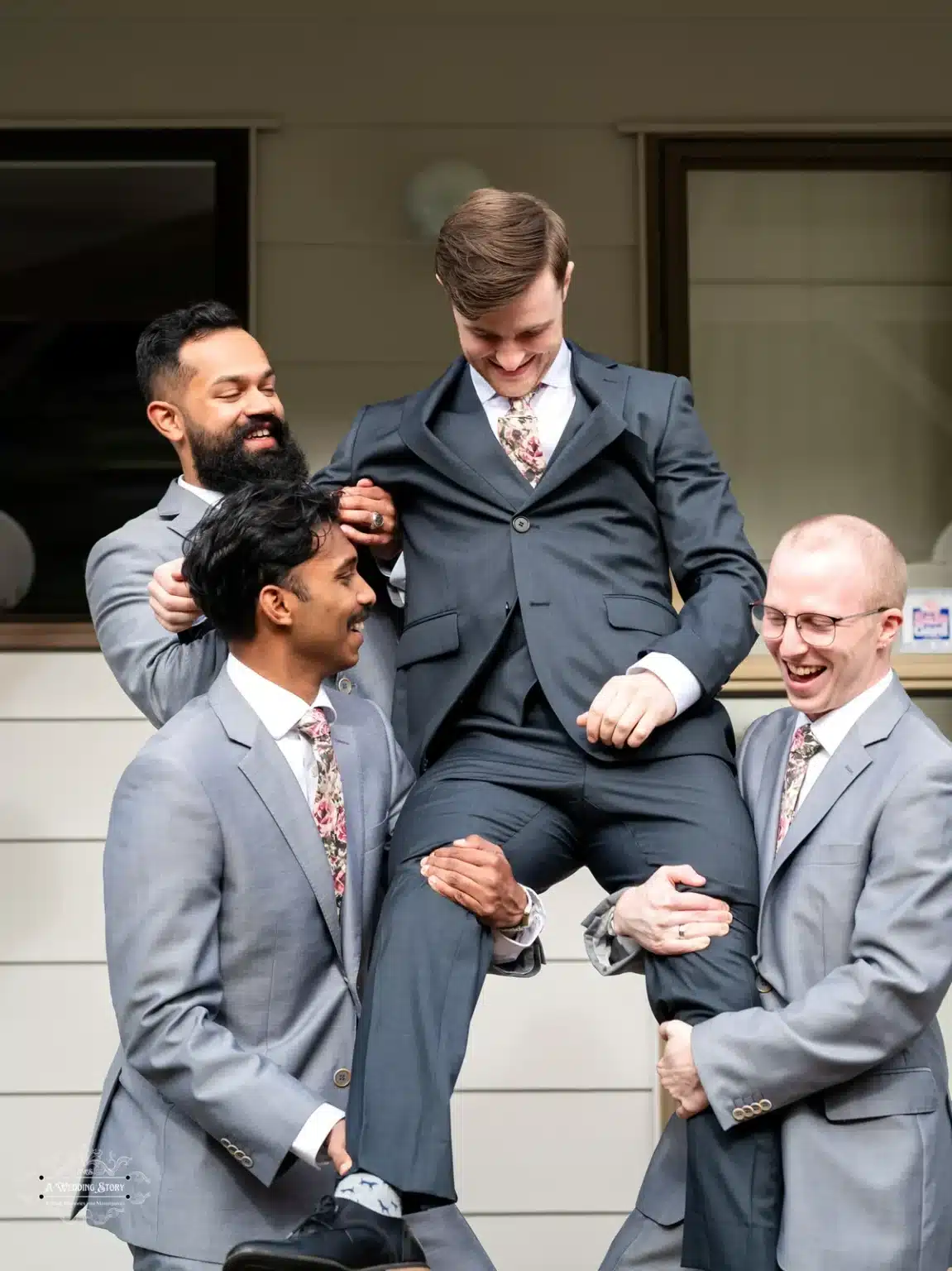 Candid moment of the groom being lifted by his groomsmen, dressed in grey suits and floral ties, during a wedding in Wellington, New Zealand.