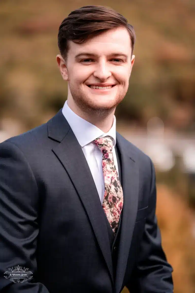 Smiling groom in a navy suit and floral tie, captured outdoors in Wellington’s picturesque setting.