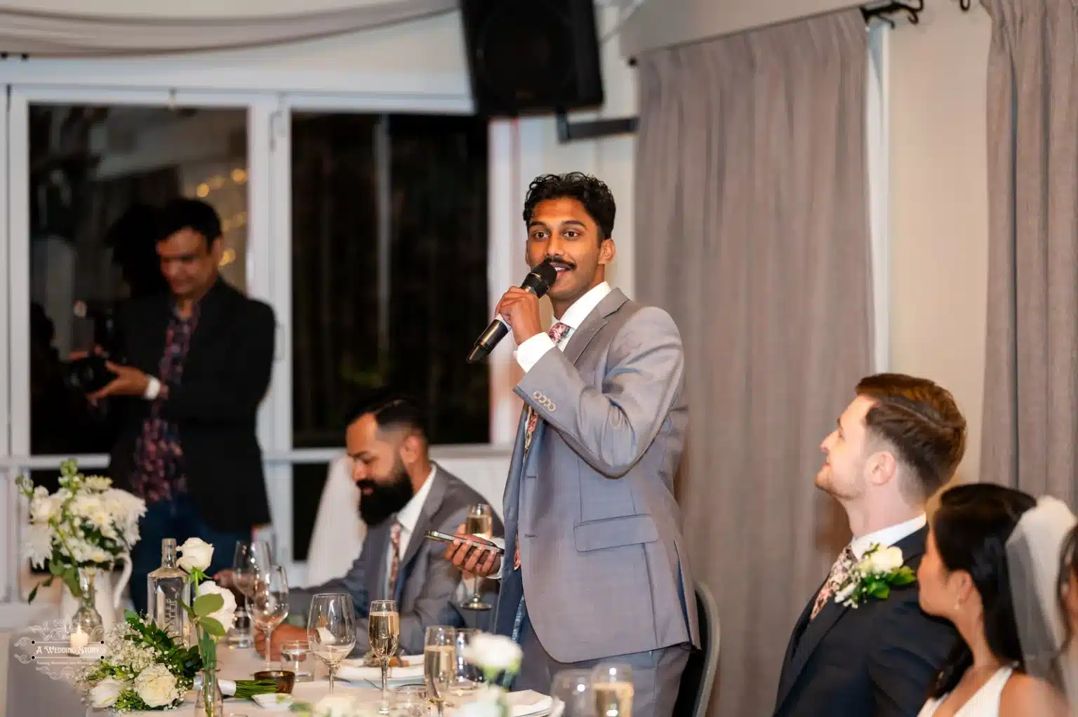 Groomsman giving a speech at the wedding reception in Wellington with guests in attendance.