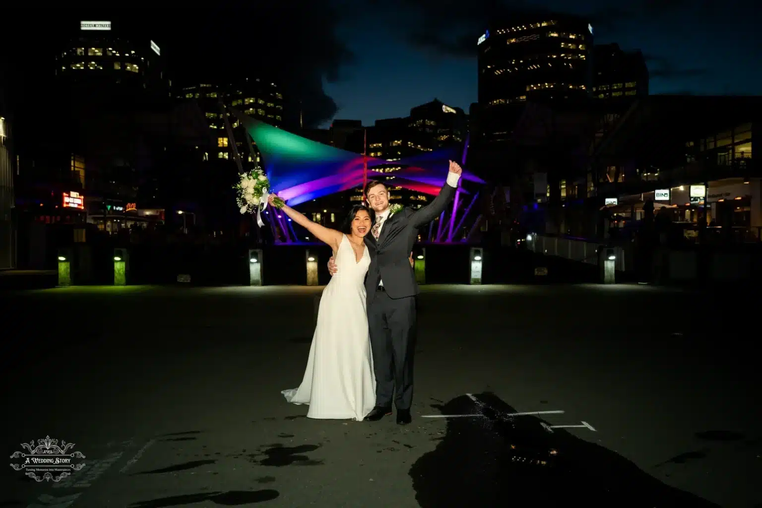 Bride and groom celebrating their wedding with vibrant city lights and colorful architectural features in Wellington at night.