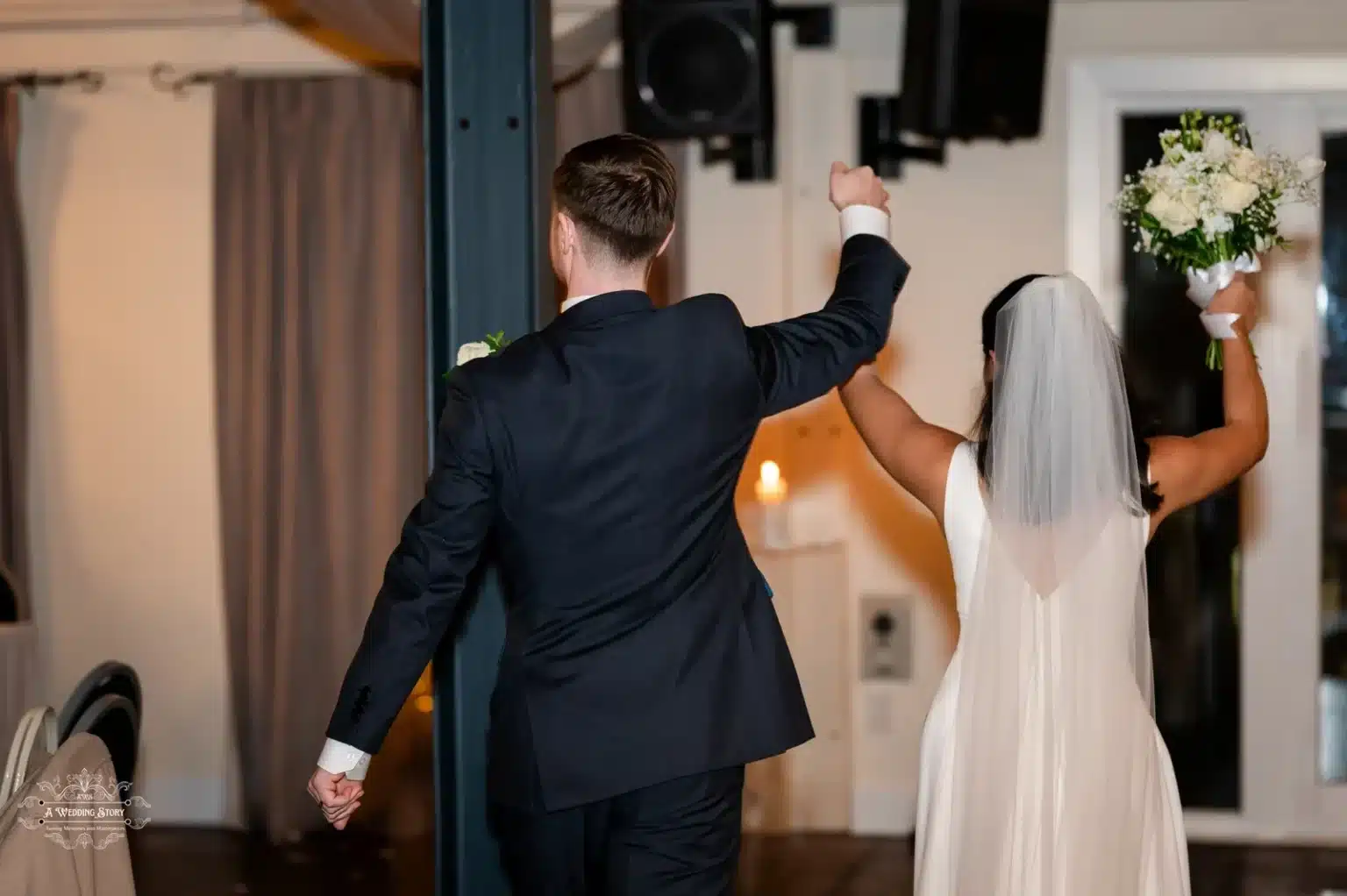 Newlyweds walking hand-in-hand at their wedding reception, bride holding bouquet.