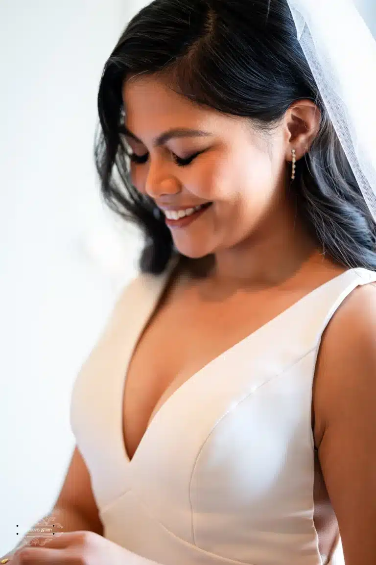 A close-up of a bride smiling gracefully as she prepares for her wedding day. She wears a simple yet elegant white gown and a delicate veil, exuding natural beauty and happiness.